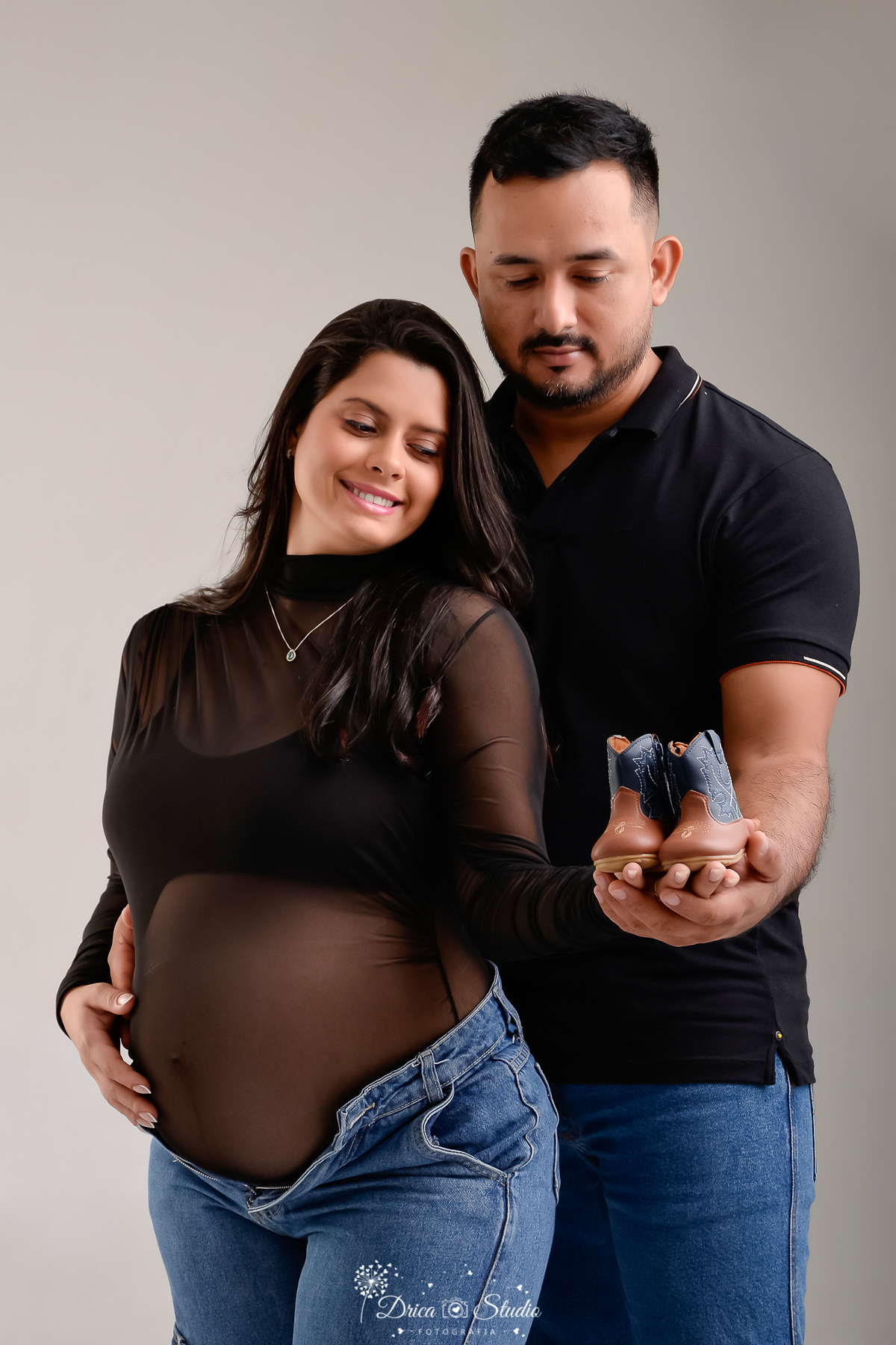 drica studio - xinguara - pará - casal - mamãe usando bory de renda preto -  papai usando camisa preta - segurando batinha do baby que está no forninho 