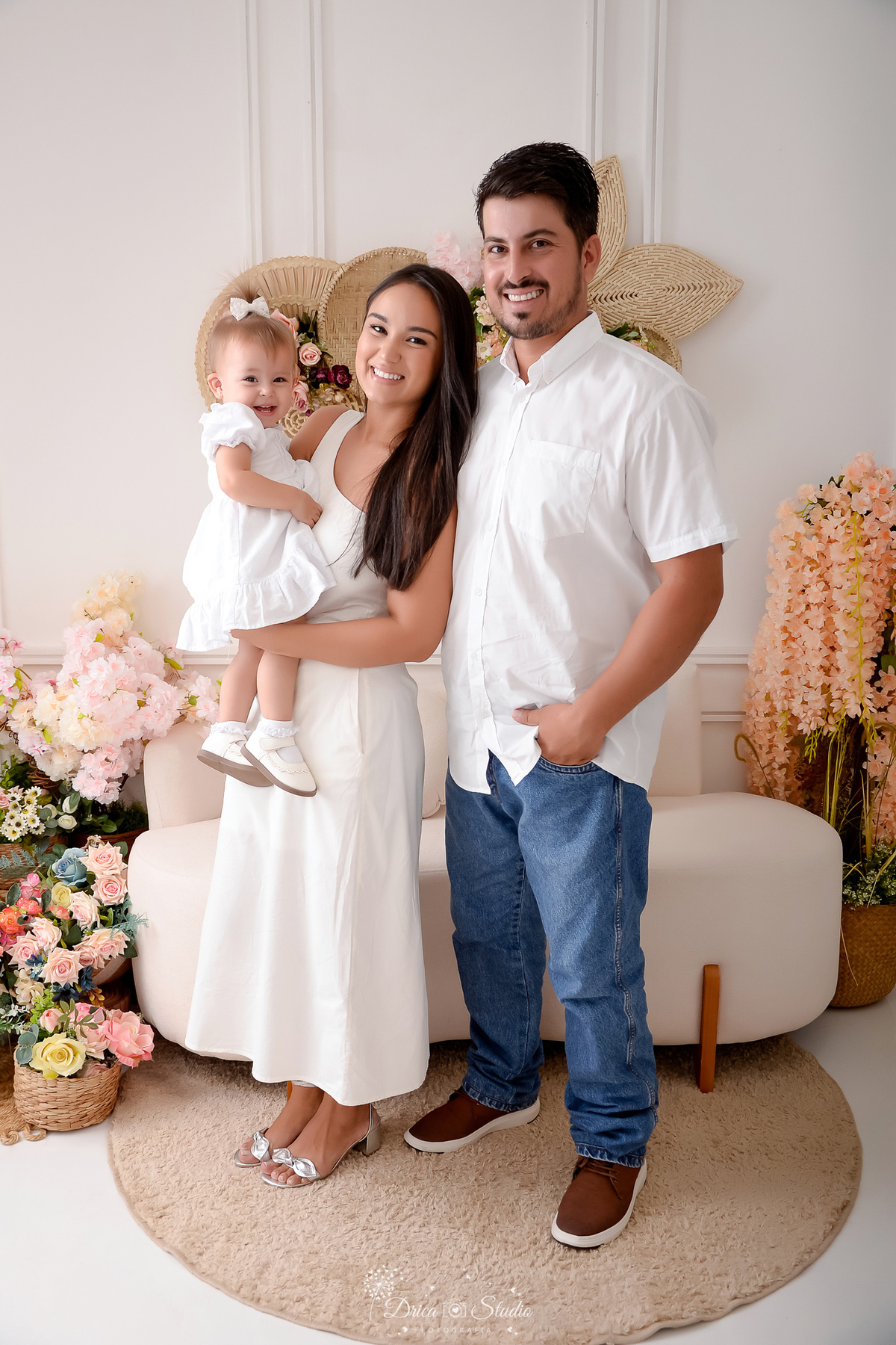 drica studio - fotos familia - xinguara - pará - familia - mamãe - papai - e filha - cenário com flores ao fundo - familia usando roupas na cor branca 