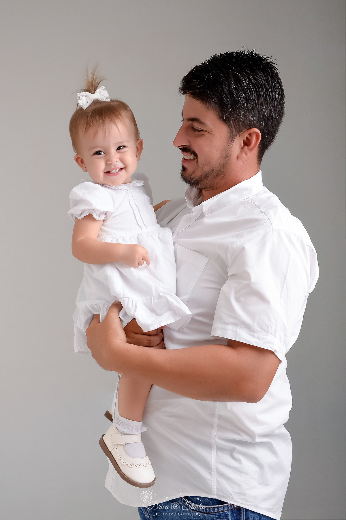 drica studio - fotos familia - xinguara - pará - pai e filha - foto estudio - fundo branco - papai e bebê usando roupas brancas - pai olhando para a finha - bebê sorrindo 