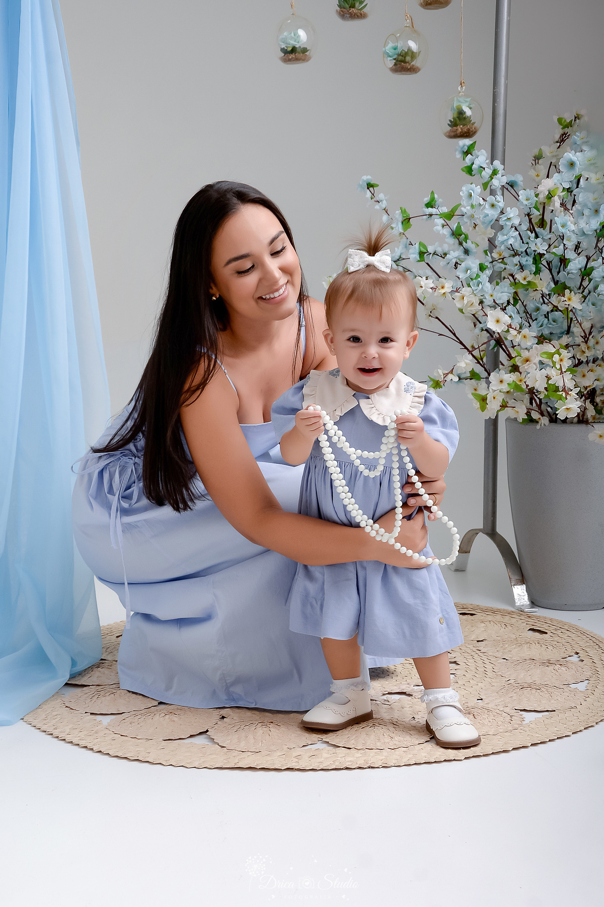 drica studio - fotos familia - xinguara - pará - mãe e finha - usando vestidos azuis - foto estudio - ao fundo flores azuis - mãe olhando para a filha 