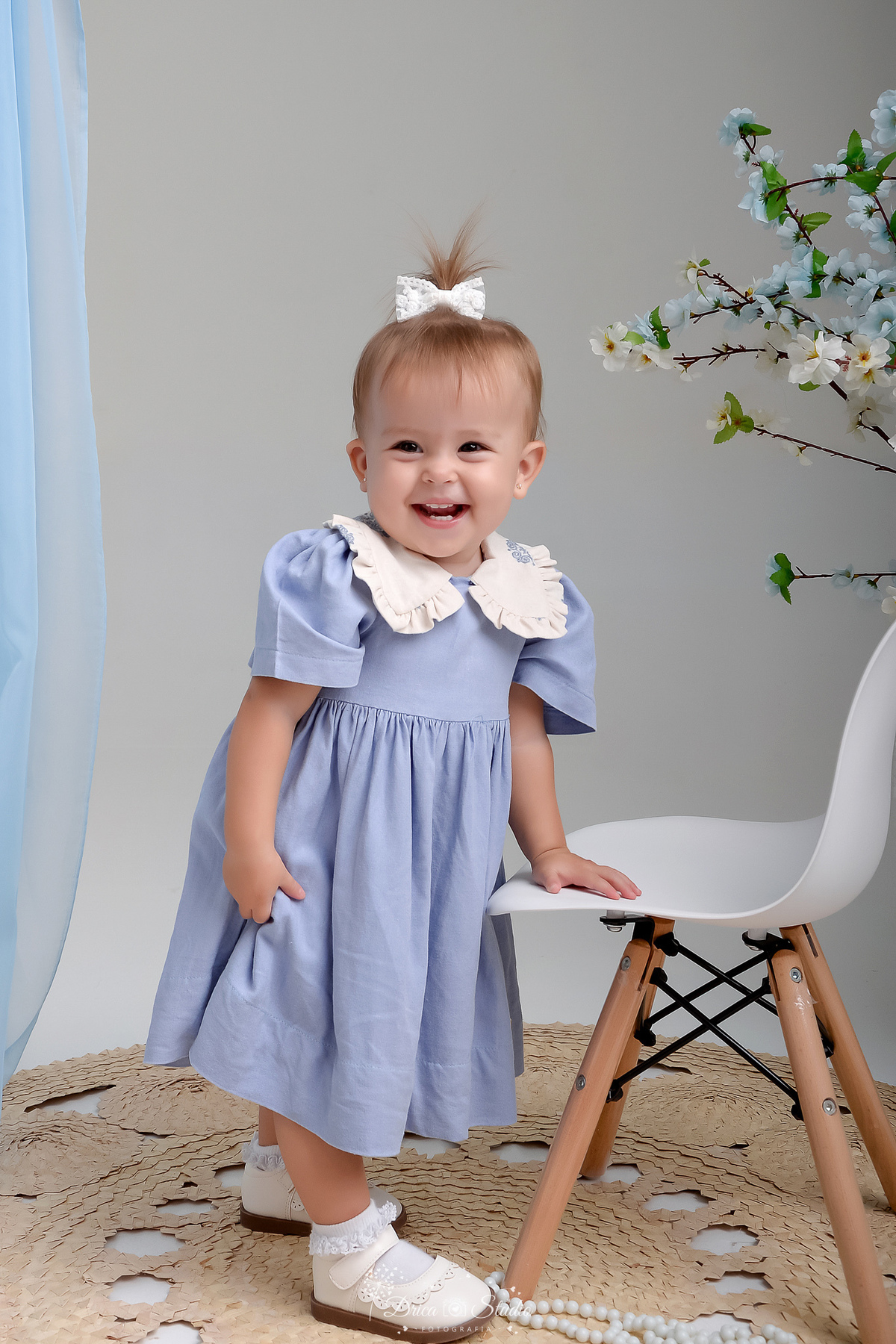 drica studio - fotos familia - xinguara - pará - bebê sorrindo - segurando em uma mini cadeira - usando vestido azul - bebê carismatica e sorridente 