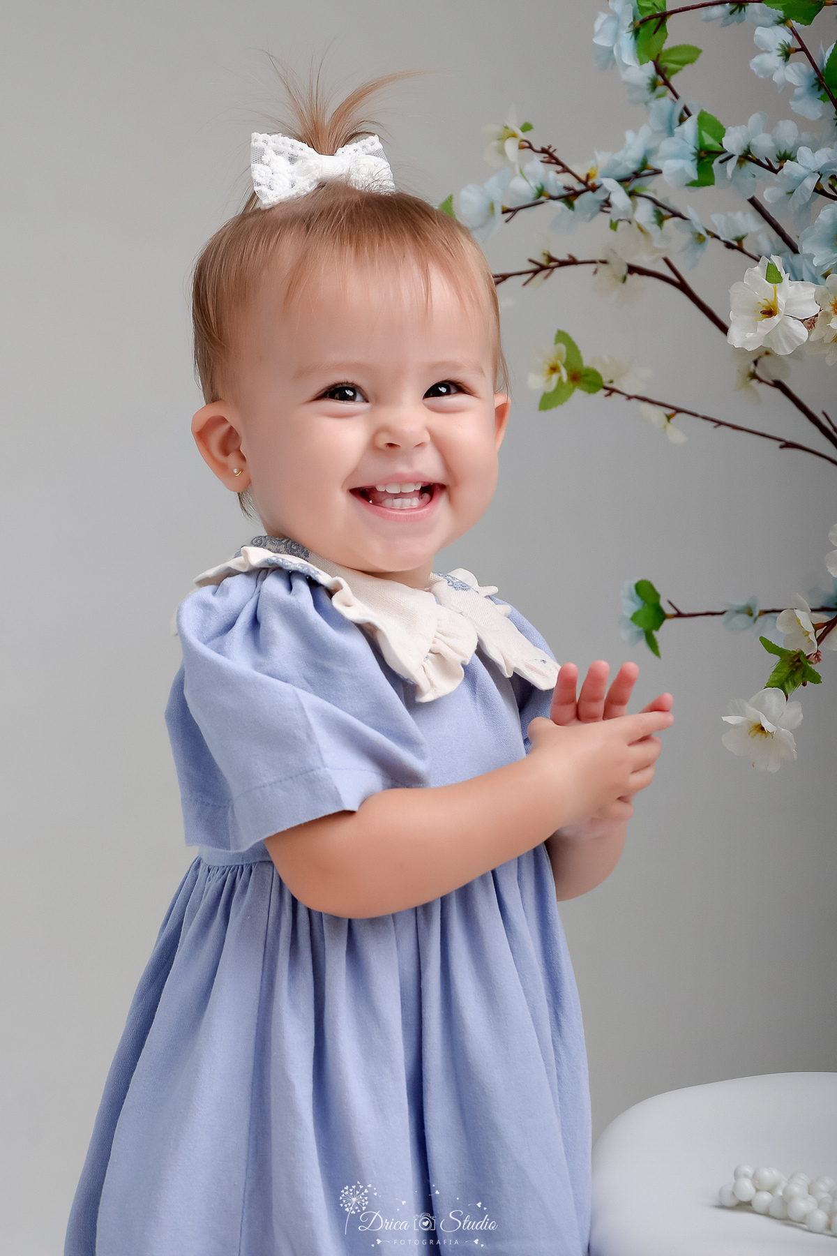 drica studio - fotos familia - xinguara - pará - bebê sorrindo - pegando nas mãozinhas - ao fundo flores azuis  - bebê usando vestido azul 