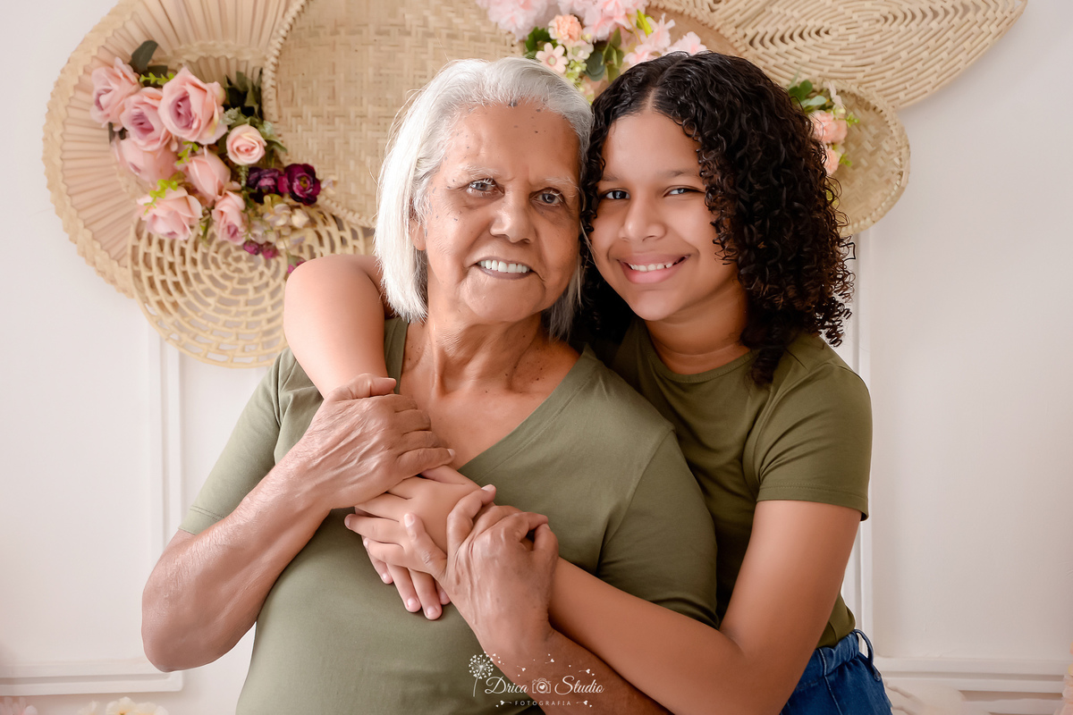 drica studio - ensaio familia - 4 gerações - bizavó - avó - mãe - filha - bizavó e neta juntas - abraçadas - usando camisas verdes no mesmo tom - e calça jeans - flores ao fundo 