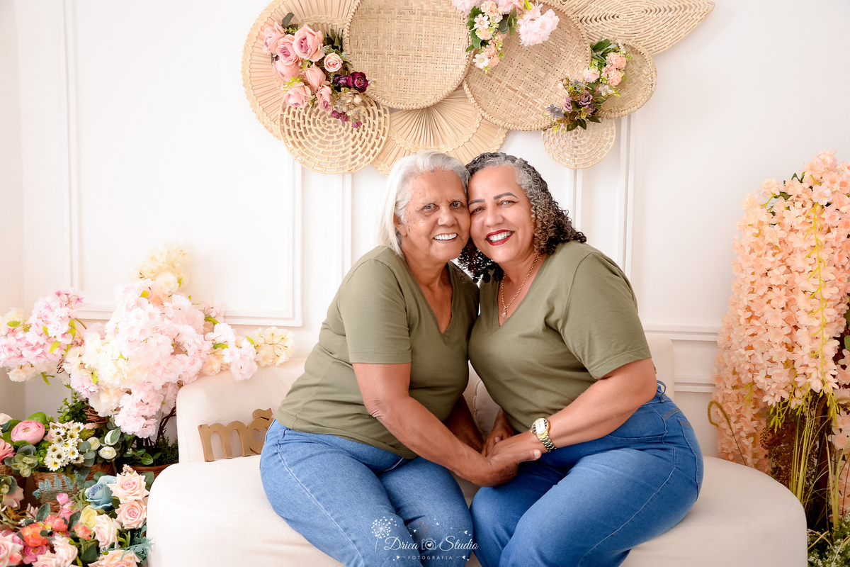 drica studio - ensaio familia - 4 gerações - bizavó - avó - mãe - filha - mãe e filha juntas - sentadas em sofá - fundo branco com flores ao fundo - usando camisas verde no mesmo tom - e calça jeans 