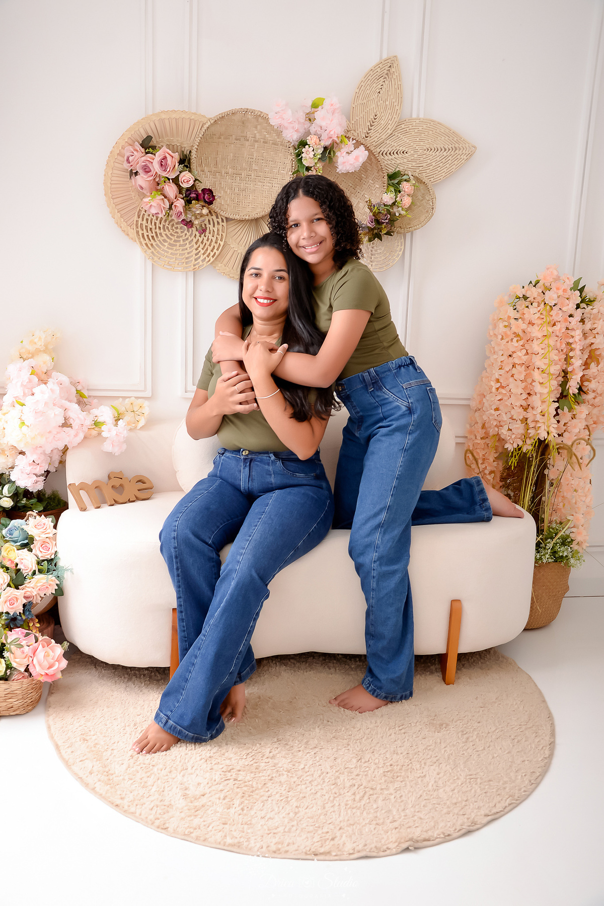 drica studio - ensaio familia - 4 gerações - bizavó - avó - mãe - filha - mãe e filha juntas - em canário de dia das mães - cenário com flores - mãe sentada sobre sofá - filha abraçando sua mãe - as duas sorrindo 