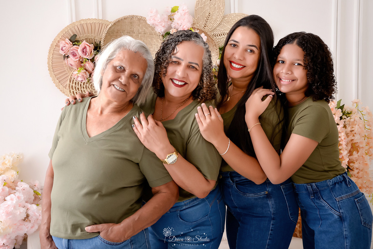 drica studio - ensaio familia - 4 gerações - bizavó - avó - mãe - filha - familia reunida - abraçadas - cenário branco com flores - familia usando camisa verde no mesmo tom  - familia feliz 