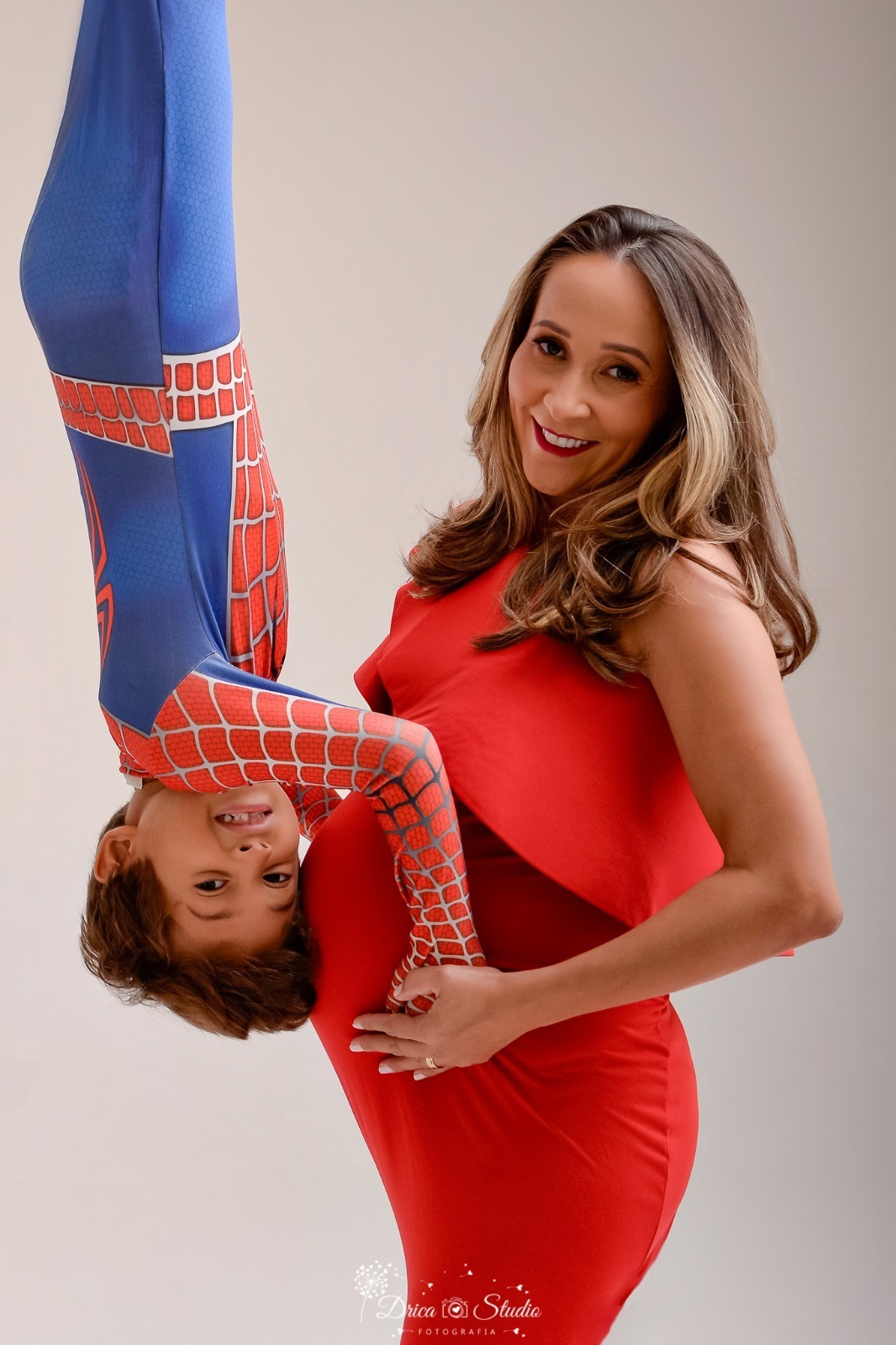 dricastudio - ensaio gestante - mamãe de segunda viagem - mãe de menino - xinguara - pará - mãe usando vestido vermelho longo - filho  usando fantasia de homem aranha - erguido ao lado da barriga da mãe - mãe e filho sorrindo 