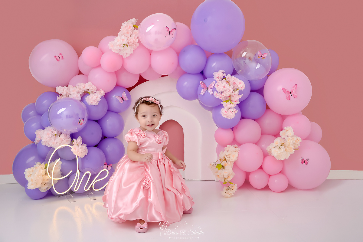 drica studio - smash the cake - jardim encantado - fotos em estudio - cenário com balões rosas e lilás - flores e borboletas - bebê usando vestido rosa - one de led 