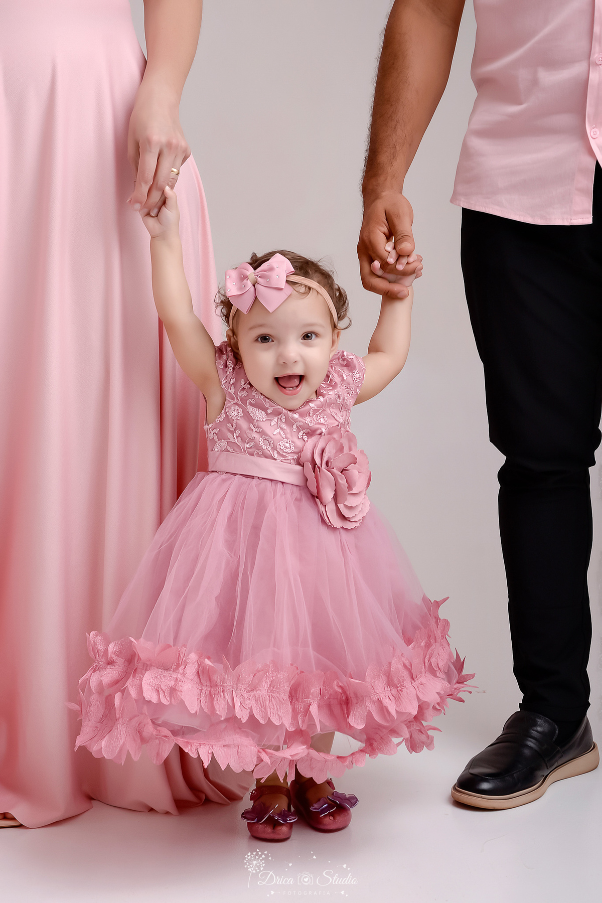 drica studio - smash the cake - jardim encantado - fotos em estudio - mamãe e papai segurando as mãozinhas da bebê - primeiros passinhos - bebê usando vestido rosa com flores 