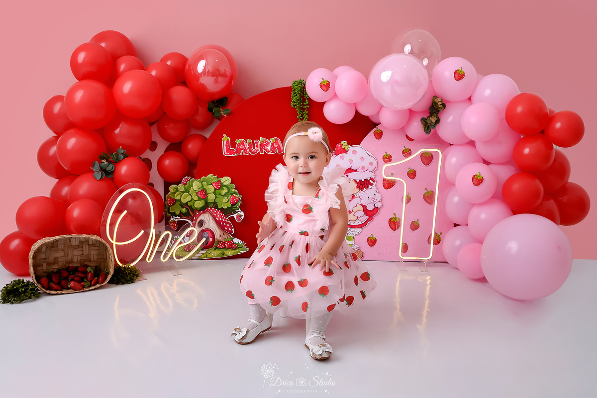 dricastudio - smash the cake - acompanhamento mensal - 1 aninho - xinguara - pará -tema moranguinho - cenário com balões rosas e vermelhos - one de led - 1 de led - monrangos pelo cenário - bebê usando vestido de morango - sentada em um baquinho  