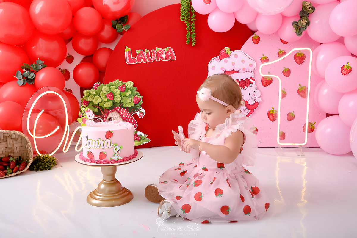 dricastudio - smash the cake - acompanhamento mensal - 1 aninho - xinguara - pará - cenário da moranguinho - balões rosas e vermelhos - one d eled - 1 de led - bebê usando vestido de moranguinho - usando laço - com as mãozinhas com bolo 