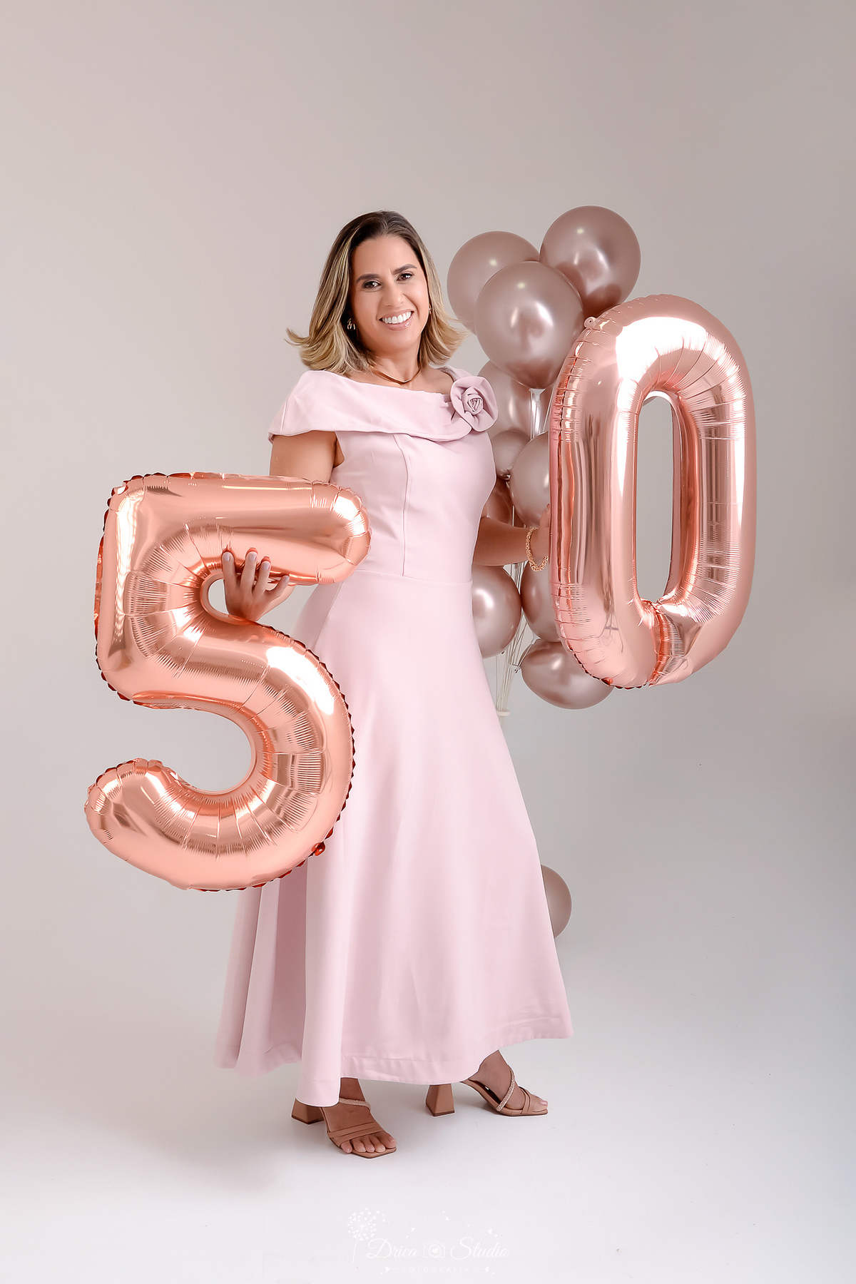 Ensaio comemorativo de 50 anos realizado em estúdio com iluminação suave e elegante.
Cliente vestindo um sofisticado vestido em tom rosa claro, transmitindo delicadeza e feminilidade.
Sorriso espontâneo e acolhedor, 