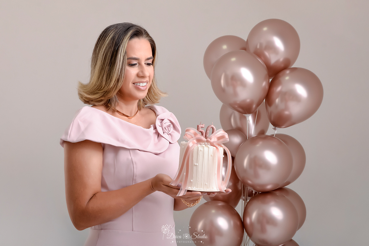 Ensaio comemorativo de 50 anos realizado em estúdio com iluminação suave e elegante.
Cliente vestindo um sofisticado vestido em tom rosa claro, transmitindo delicadeza e feminilidade.
Sorriso espontâneo e acolhedor, 