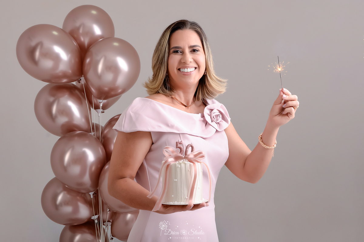 Ensaio comemorativo de 50 anos realizado em estúdio com iluminação suave e elegante.
Cliente vestindo um sofisticado vestido em tom rosa claro, transmitindo delicadeza e feminilidade.
Sorriso espontâneo e acolhedor, 