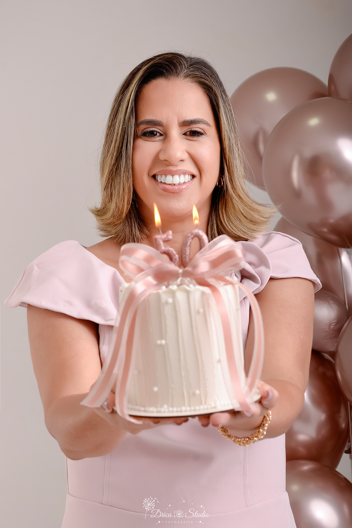 Ensaio comemorativo de 50 anos realizado em estúdio com iluminação suave e elegante.
Cliente vestindo um sofisticado vestido em tom rosa claro, transmitindo delicadeza e feminilidade.
Sorriso espontâneo e acolhedor, 