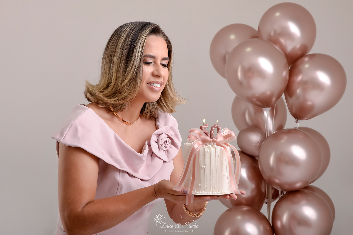 Ensaio comemorativo de 50 anos realizado em estúdio com iluminação suave e elegante.
Cliente vestindo um sofisticado vestido em tom rosa claro, transmitindo delicadeza e feminilidade.
Sorriso espontâneo e acolhedor, 