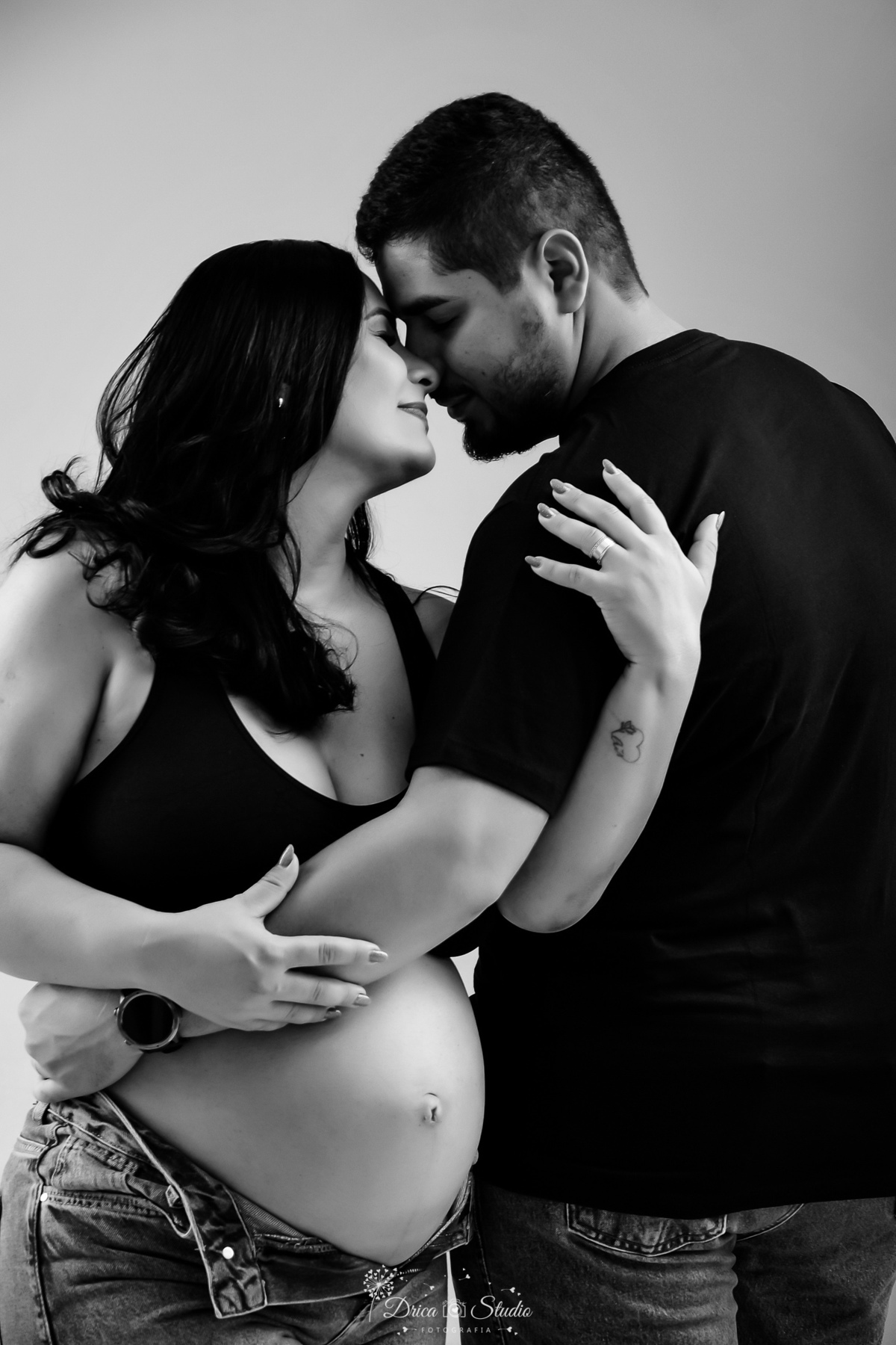 EnsaioGestante - MeninaACaminho - ÀEsperaDaPrincesa - PrimeiraFilha - FotografiaGestante Família - Gestação - MemóriasParaSempre - drica studio - fotos em studio gestante usando calça jeans e tope preto - foto em fundo branco - esposo usando camisa preta