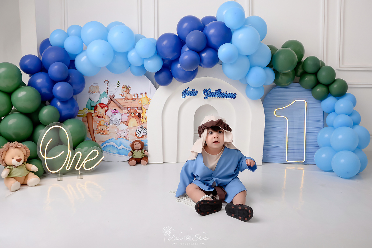 drica studio - smash the cake - tema arca de nóe - balões azuis e verde - one de led - 1 de led - fundo branco - imagem da arca de noé ao fundo  - bebê com a roupinha de noé 