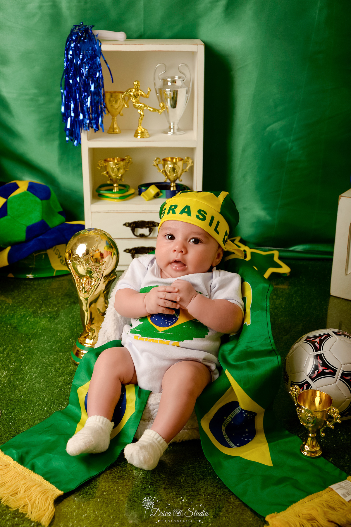 Drica Studio - Copa2026 -Lembrança especial primeira copa - cenário de copa - verde, amarelo e azul - bebê usando bory branco da copa - usando bandana do brasil na cabeça - com taça da copa ao lado 