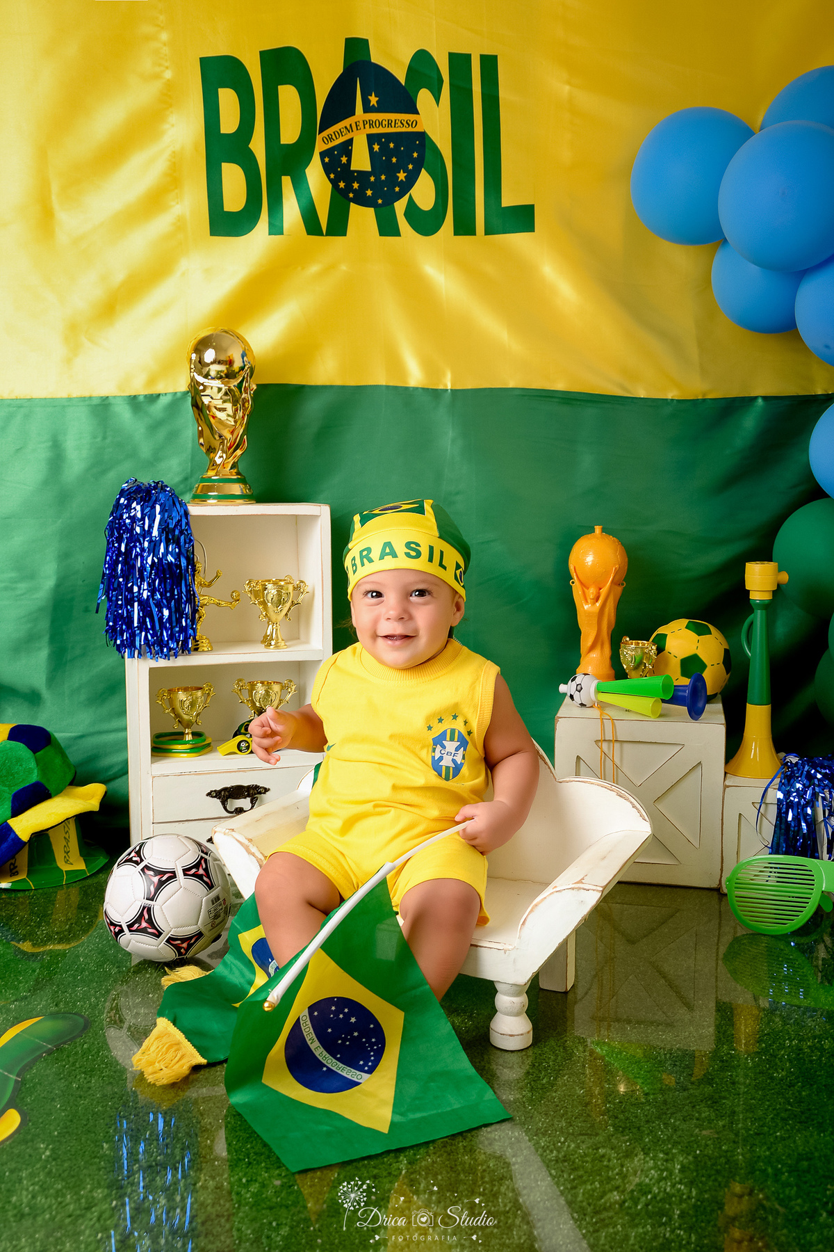 Drica Studio - Copa2026 -Lembrança especial primeira copa - cenário de copa - verde, amarelo e azul - bebê sentado num baquinho - usando bory amarelo - segurando uma bandeira do brasil e bandana 