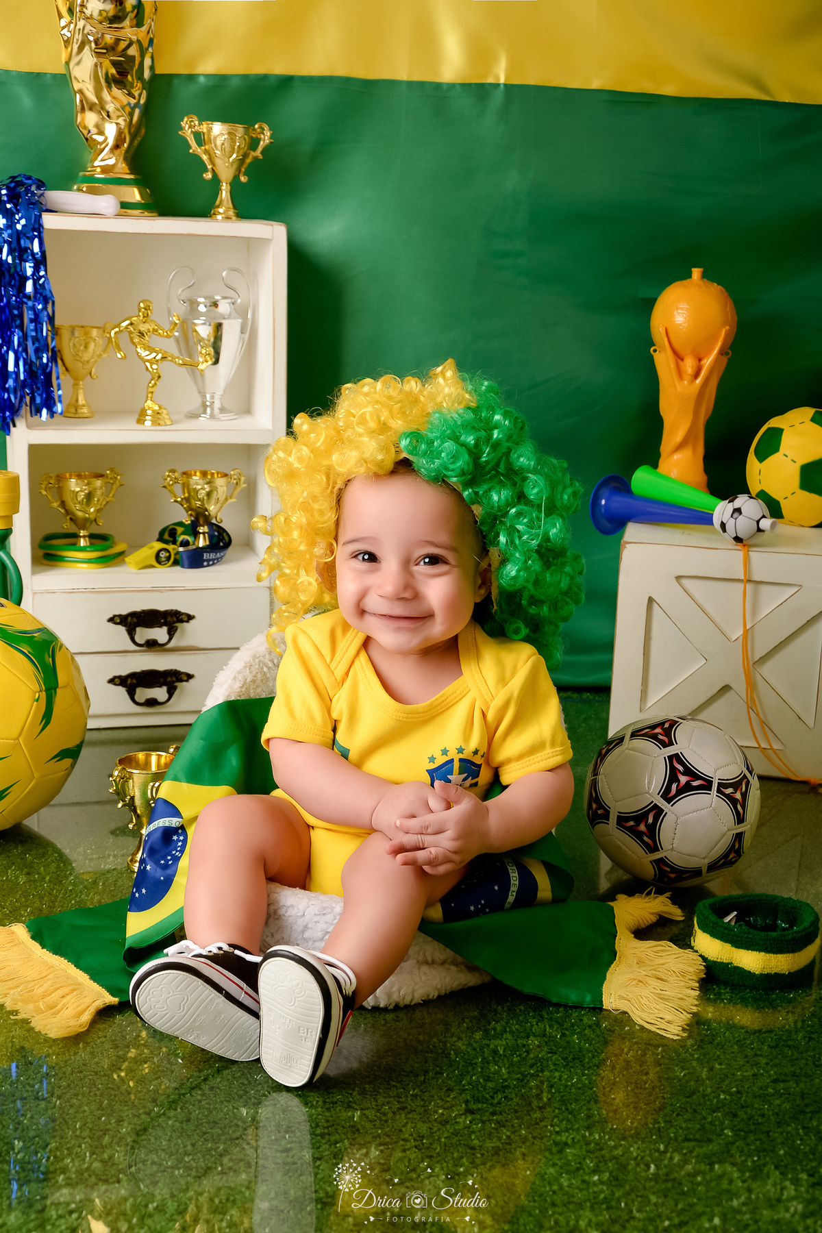 Drica Studio - Copa2026 -Lembrança especial primeira copa - cenário de copa - verde, amarelo e azul -  bebê usando bory amarelo - e peruca verde e amarela -  sentado em uma cadeirinha - com bola de futbol ao lado - sorrindo 
