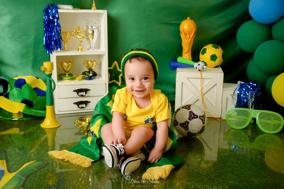 Drica Studio - Copa2026 -Lembrança especial primeira copa - cenário de copa - verde, amarelo e azul - bebê usando bory amarelo do brasil - sentado em uma cadeirinha no cenário de copa - usando tenis alstar