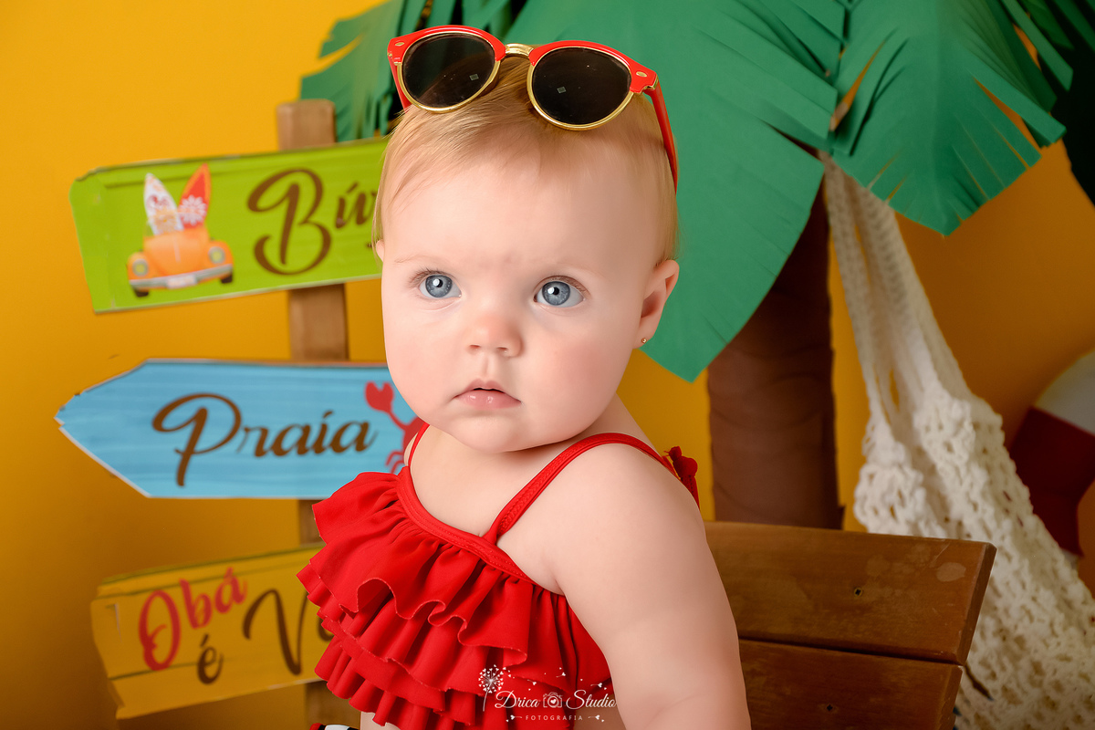 verão2026 - cenário de praia - acompanhamento mesal - drica studio - xinguara - pará - bebê com oculos na cabeça - ao fundo um coqueiro marrom com verde 