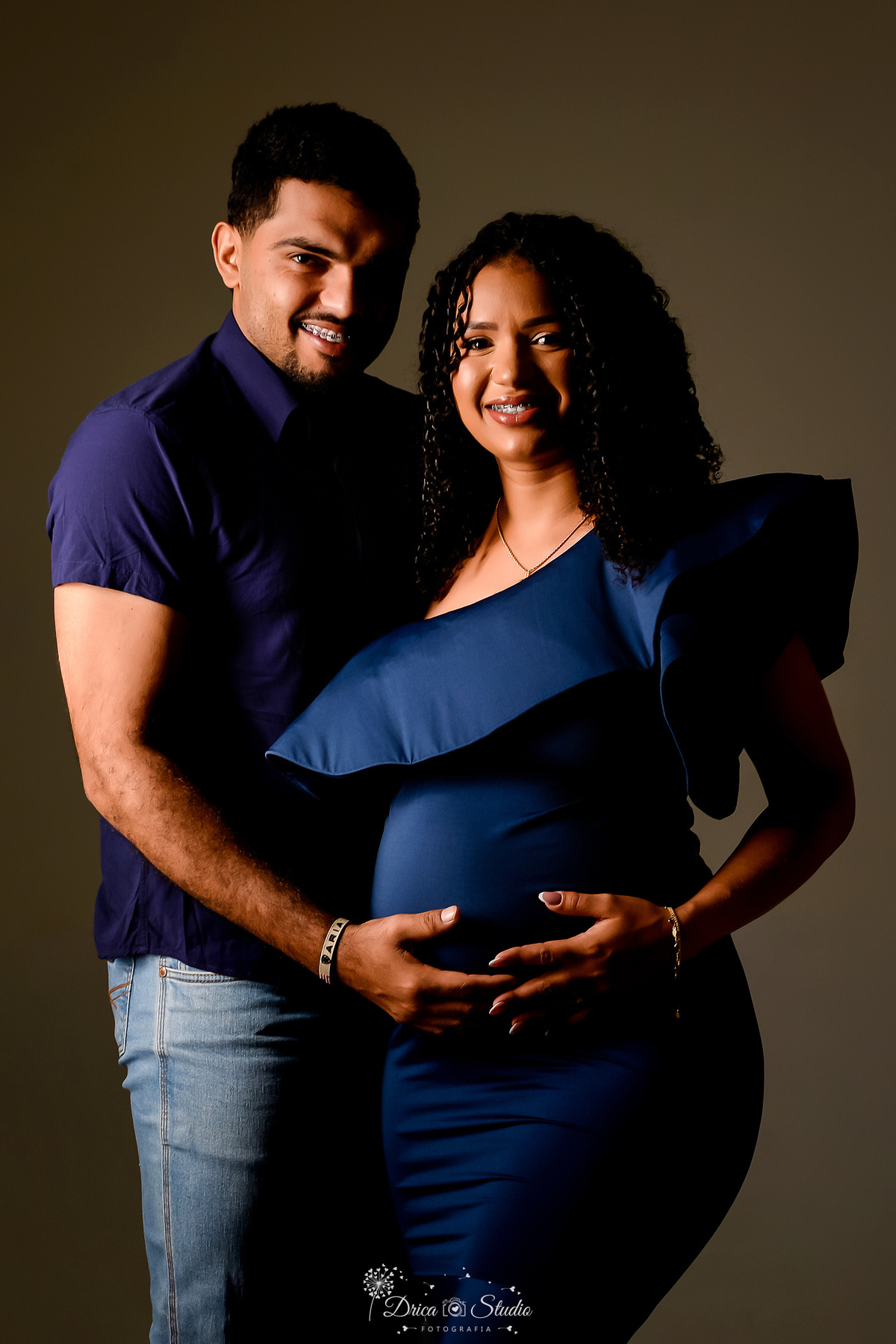 drica studio - ensaio gestante - primeiro filho - fotos em estudio - xinguara - pará - nãe usandp vestido azul - pai com camisa azul - com as mãos sobre a barriga 