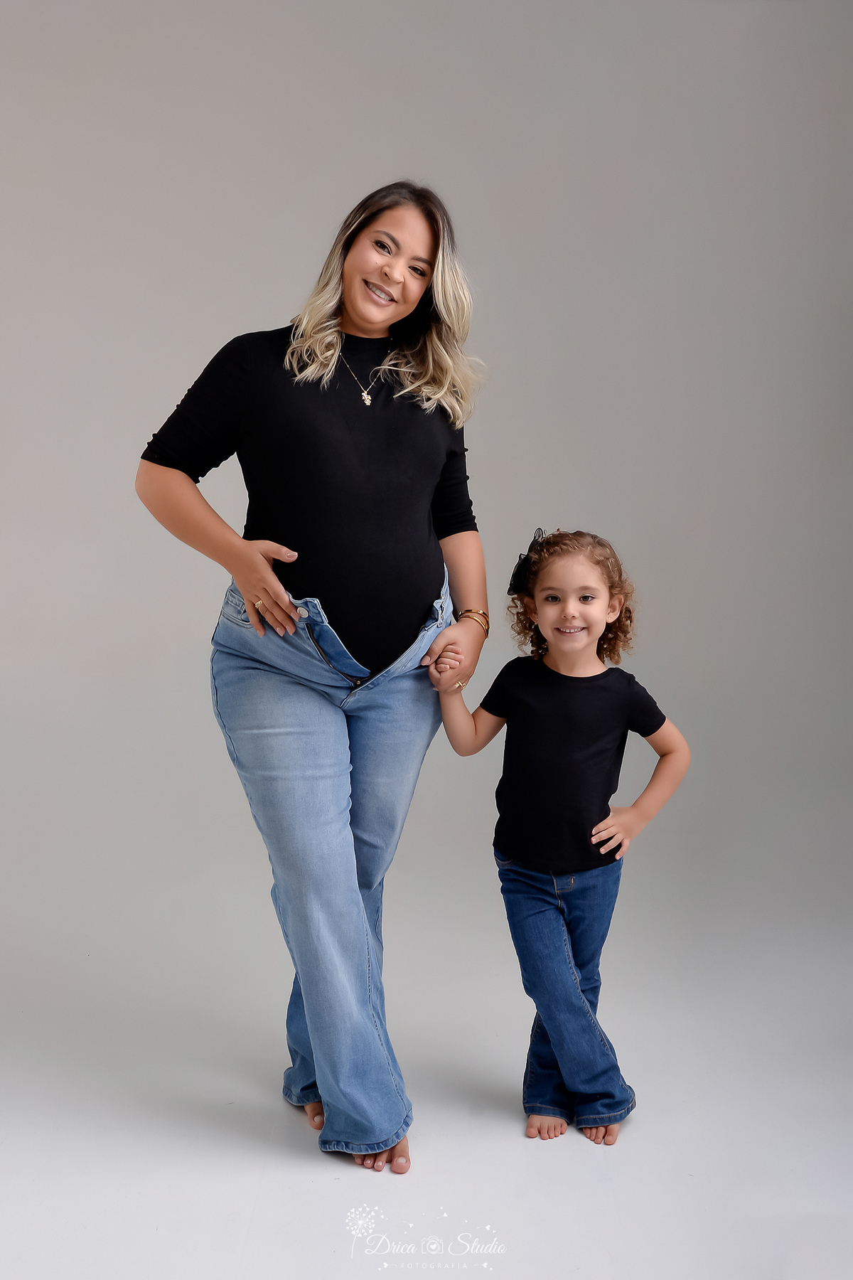 ensaio familia - ensaio gestante - mãe de 2 - irmã mais velha - ensaio em studio - xinguara -pará - mãe e filha - usando calça jeans e camisa preta - mamãe com a mão na barriga - foto em fundo branco - 