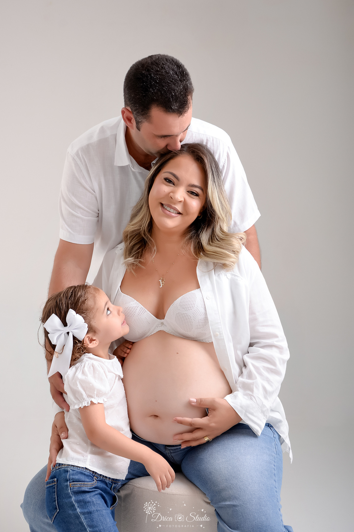 ensaio familia - ensaio gestante - mãe de 2 - irmã mais velha - ensaio em studio - xinguara -pará - familia usando calça jeans e camisas brancas - filha olhando para a mãe - pai abraçando a mãe - foto em fundo branco 