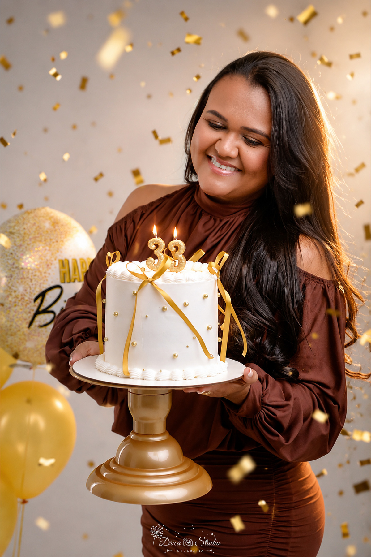 Aniversário - 33Anos - HappyBirthday - EnsaioFeminino -  EnsaioDeAniversário - segurando o bolo com vales de 33 - confetes dourados caindo - aniversariante usando vestido marrom - olhando para o bolo - 