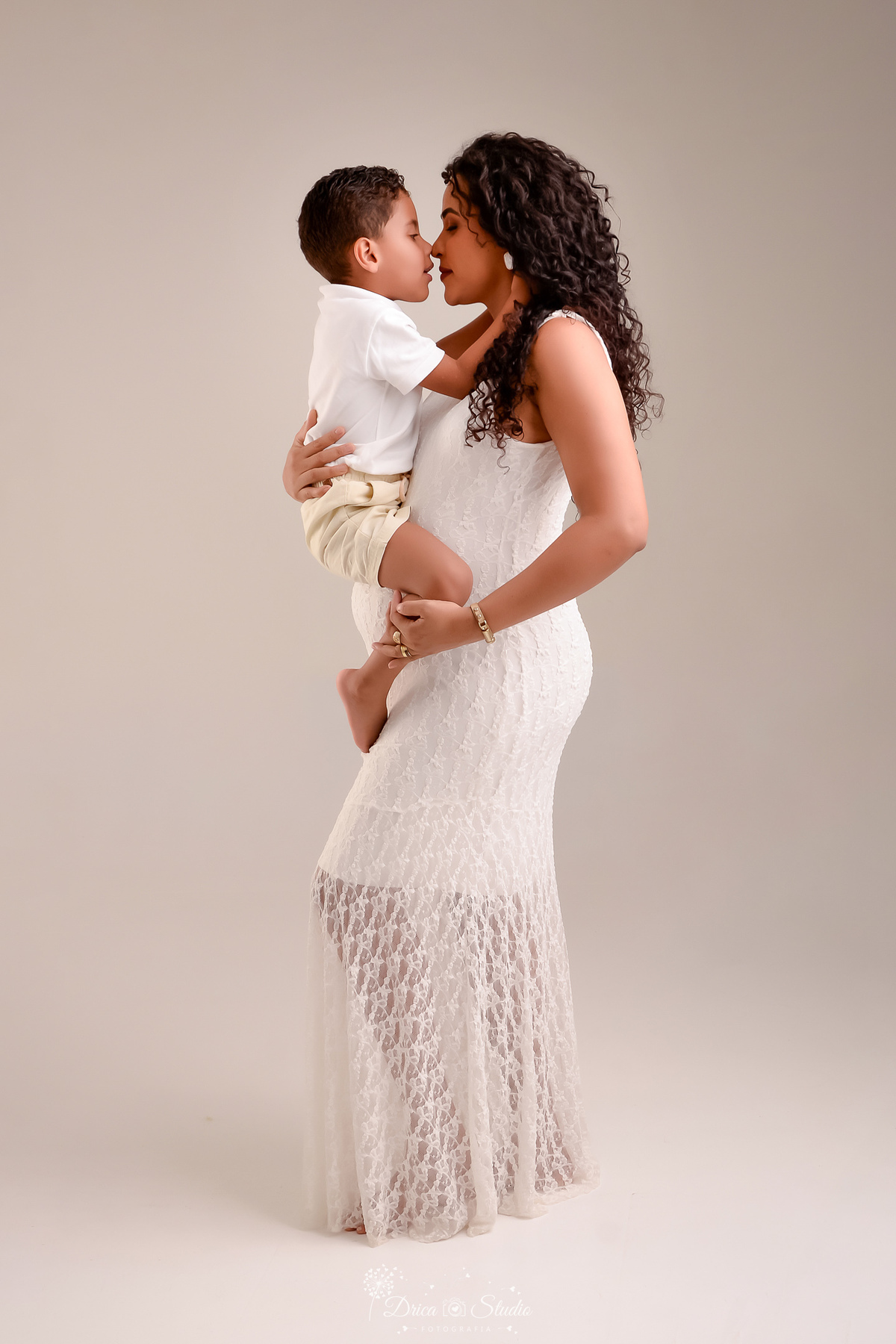 drica studio - ensaio gestante - mãe e filho - mãe de segunda viagem - usando vestido branco longo - segurando o filho mais velho no colo - foto em fundo branco - 