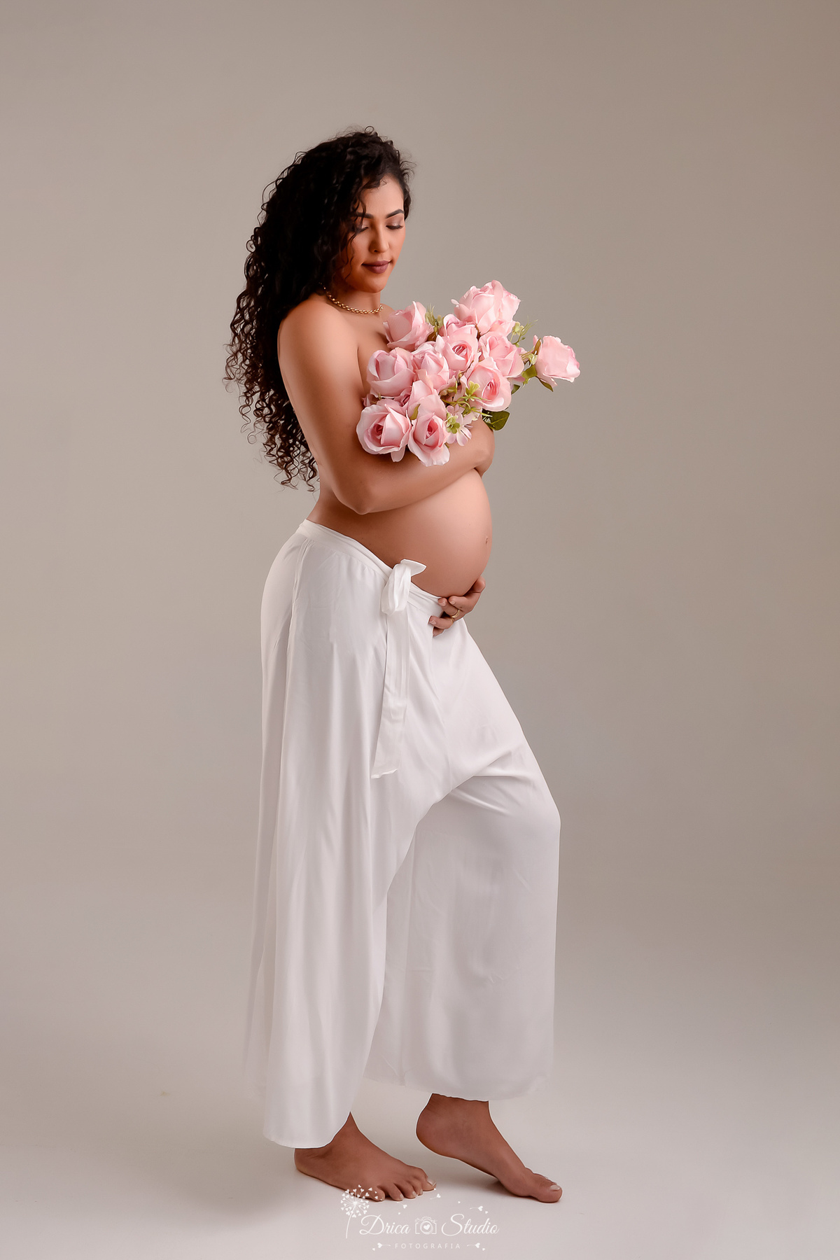 drica studio - ensaio gestante - mamãe de segunda viagem - segurando flores rosas - usando calcça de tecido branco 