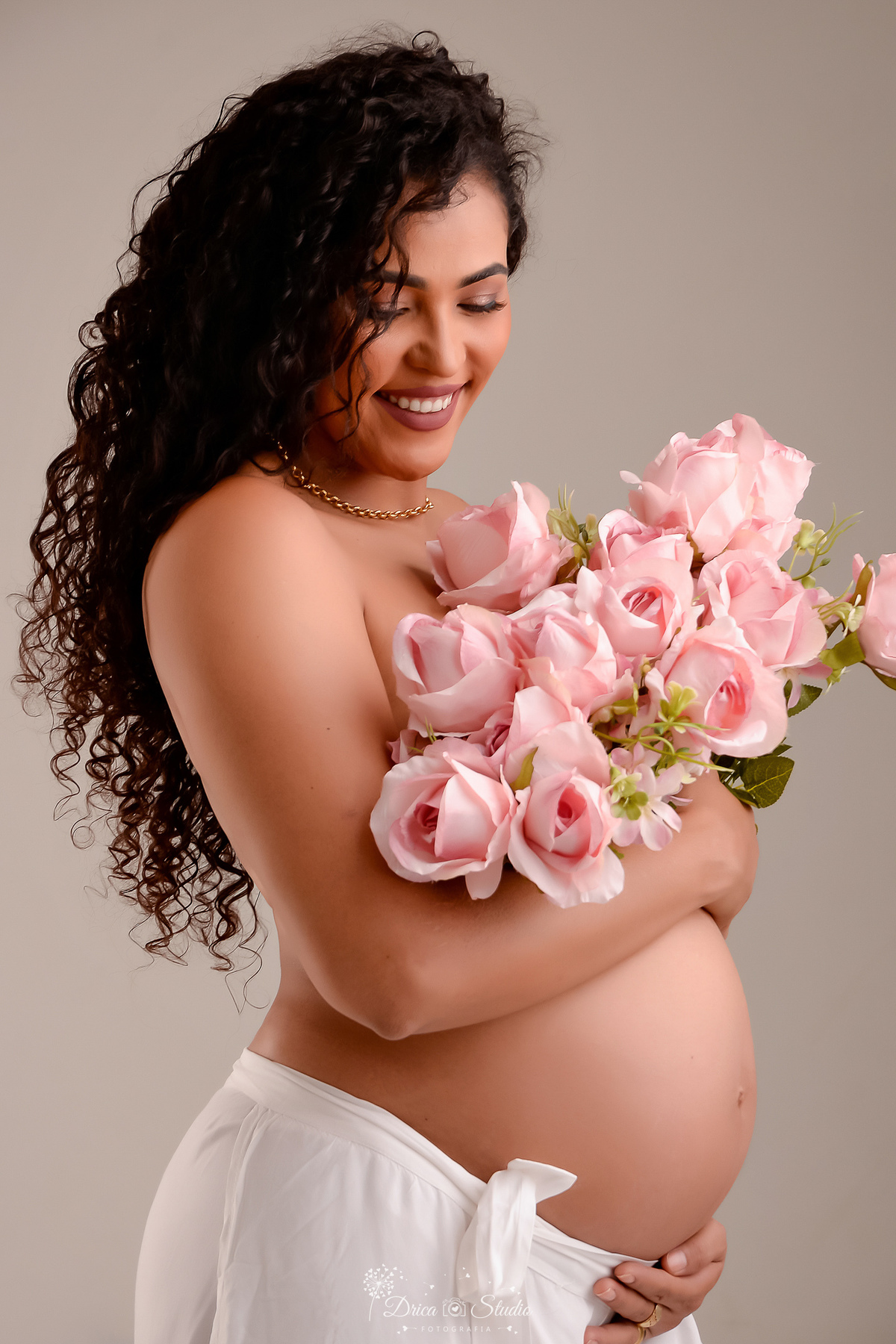 drica studio - ensaio gestante - mamãe de segunda viagem - segurando flores rosas - usando calcça de tecido branco 