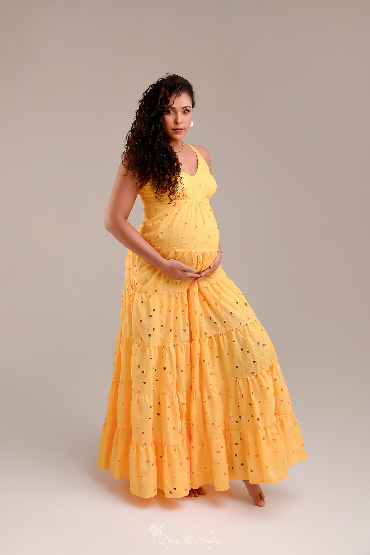 drica studio - ensaio gestante - mamãe de segunda viagem - usando vestido amarelo longo - com as mãos sobre a barriga fundo branco 