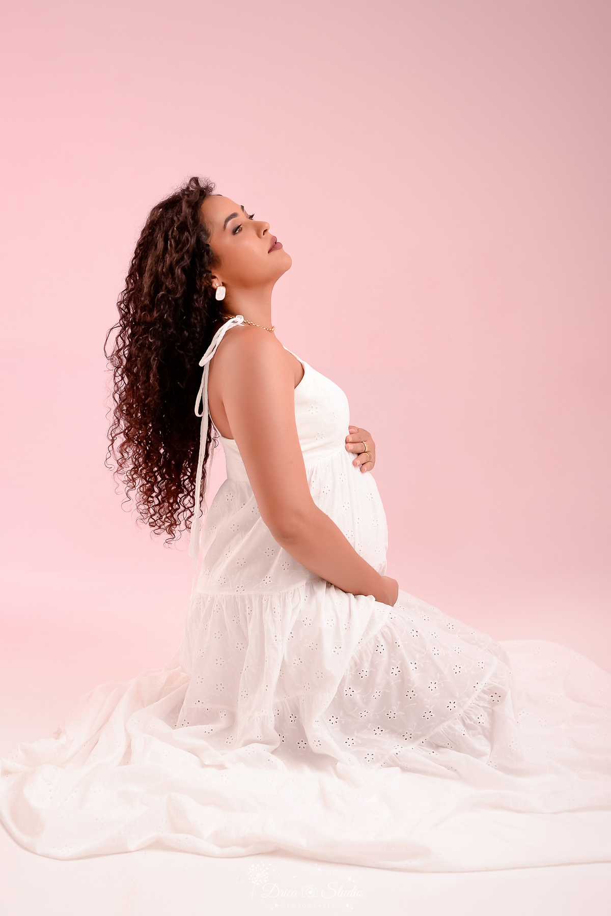 ensaio gestante - fotos em estudio - mamãe de segunda viagem - usando vestido longo branco - sentada sobre o chão - com as mãos  na barriga - 