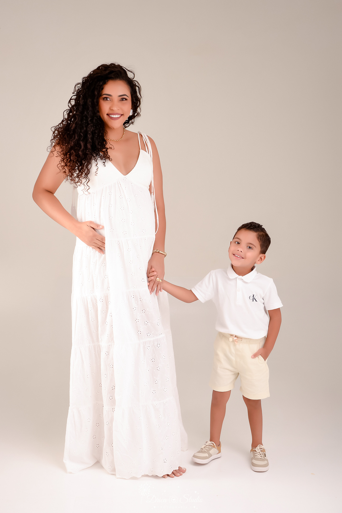 drica studio - mãe e filho - ensaio gestante - foto em estudio - mamãe de segunda viagem - usando vestido branco longo - filho usando camisa golo polo branco e bermuda - mãe e filho de mãos dadas 