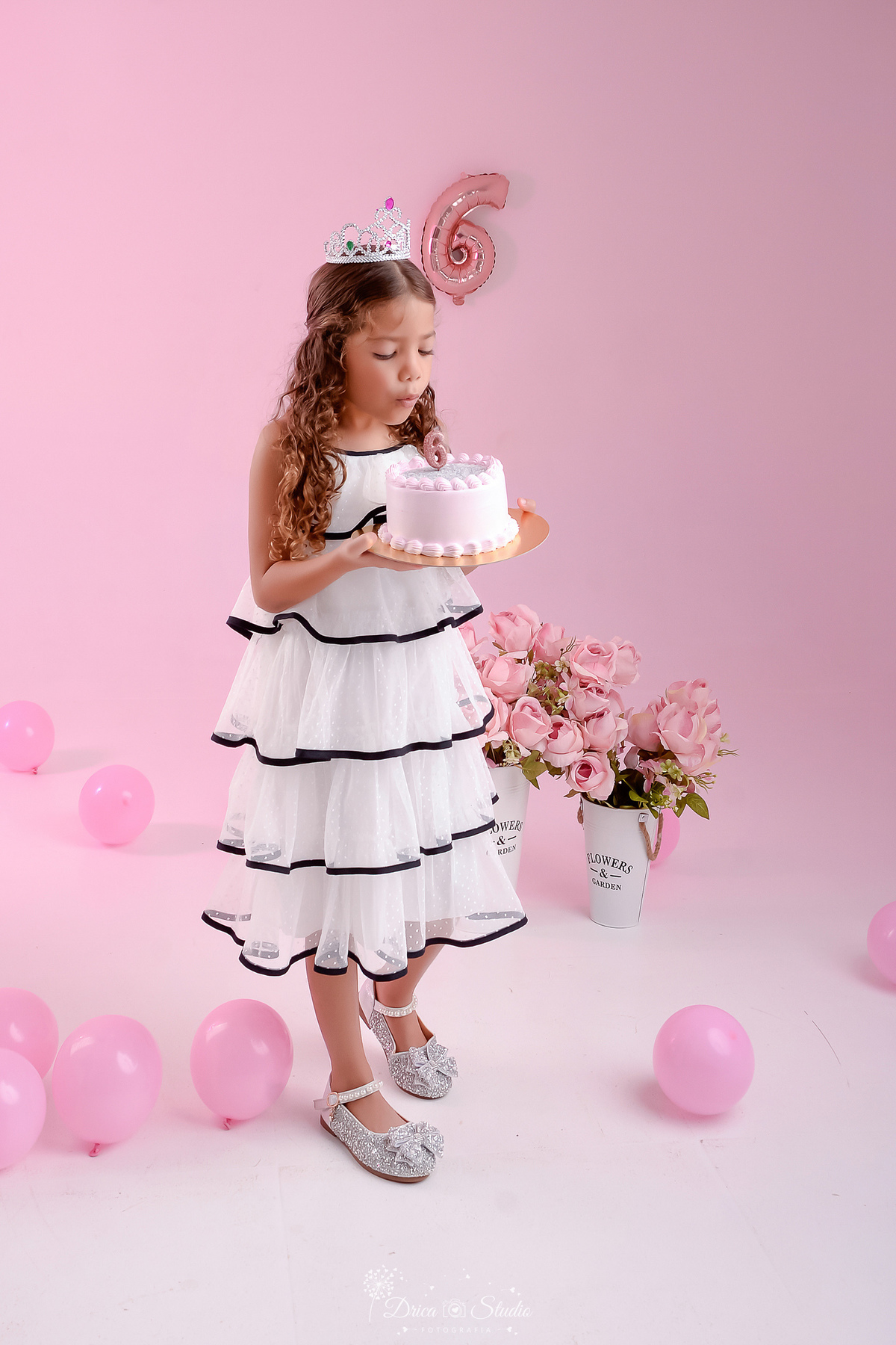 ensaio infantil - fotos de aniversario - 6 anos - menina - drica studio - xinguara - pará - foto em estudio - fundo rosa - flores rosas - balões rosas - segurando bolo - soprando a vela - usando vestido branco com detalhe preto - 