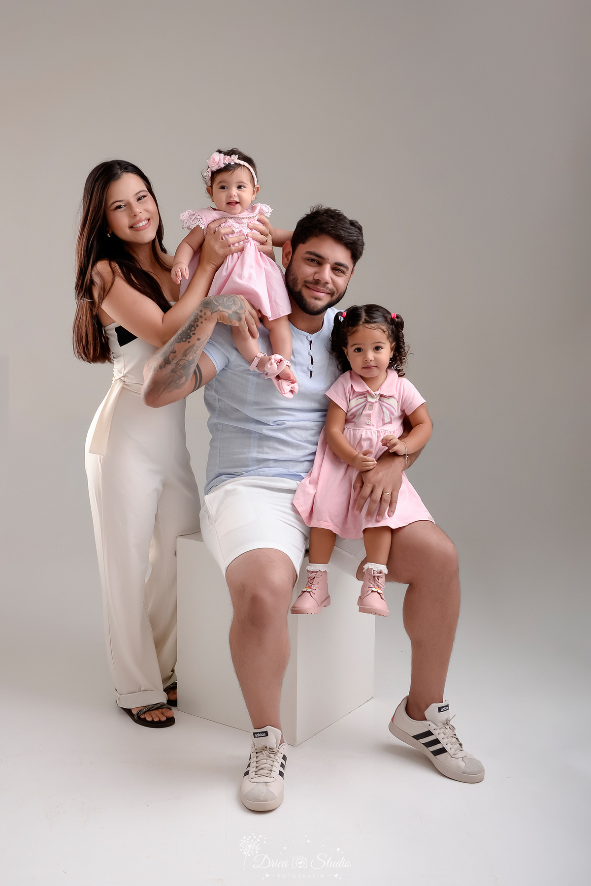 drica studio - ensaio familia - mãe pai, e filhas - foto em estudio - pai sentado em um banco segurando a filha mais velha - mãe segurando a filha caçula - familia unida