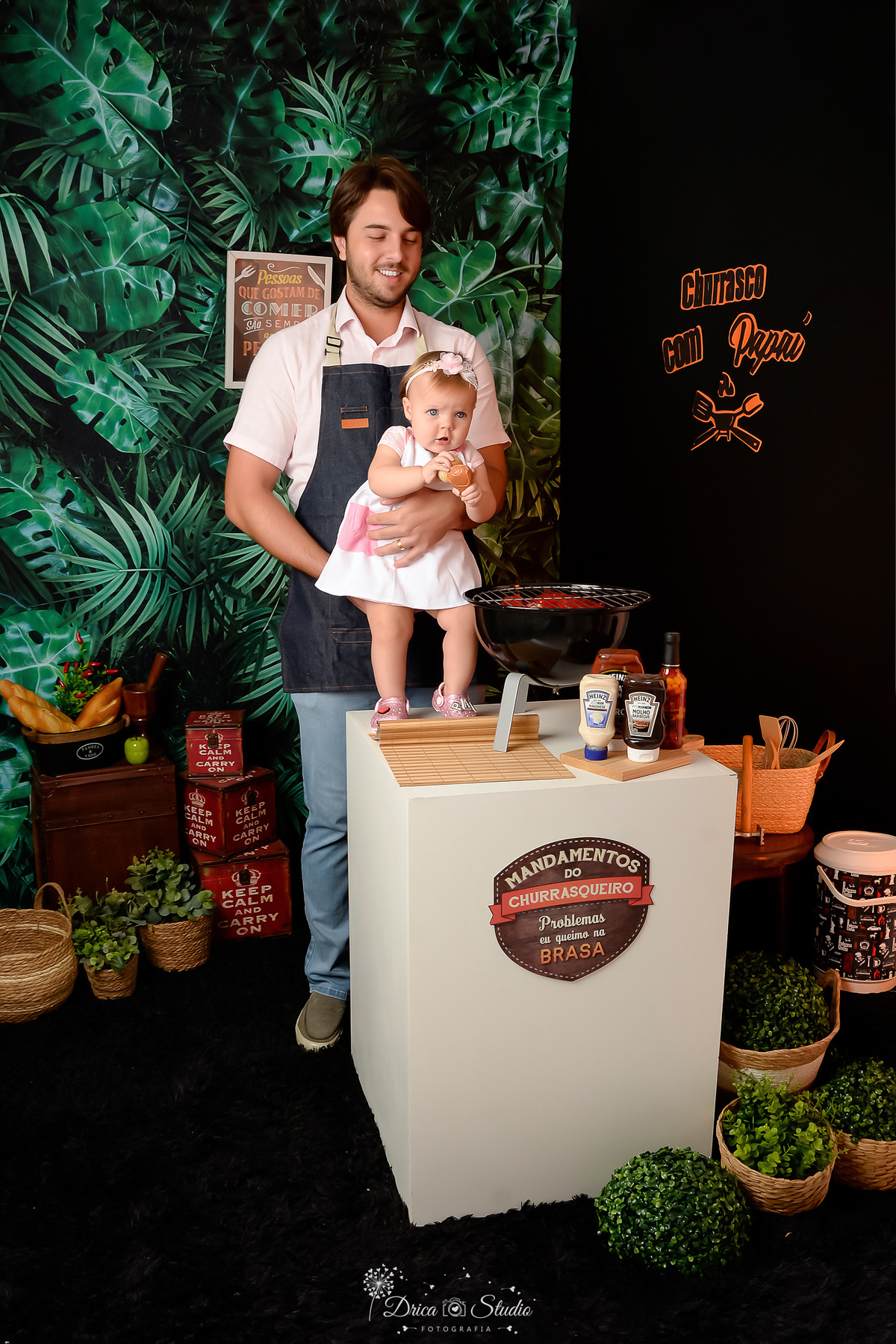 Currasco com o papai - cenario de dia dos pais - acompanhamento mensal - pai e filha - cenario com churrasqueira - molhos de churrasco - pai usando avental de churrasco - fundo com folhagens verdes e preto 