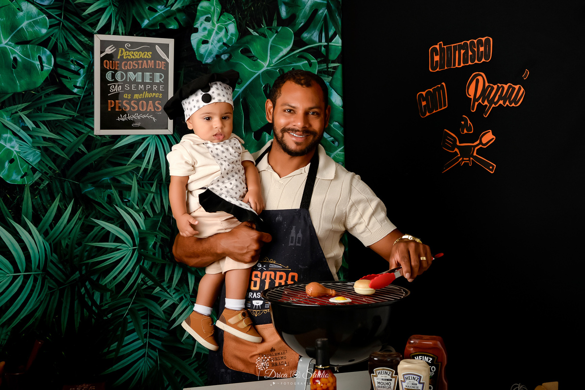 cenário de dia dos pais - cennario de churrasco - churrasqueira preta - molhos de currasco - pai e filho usando avental de churrasco - fundo com folhagens verdes - acompanhamento mensal - drica studio - xinguara - pará 