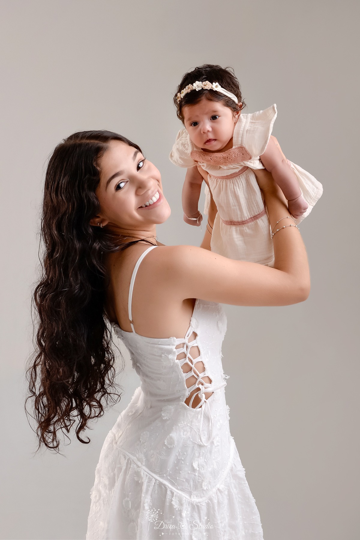 mãe e filha - acompanhamento mensal - fotos em estúdio - drica studio - xinguara - pará - mãe usando vestido branco - erguendo a filha - filha usando vestido bege - fundo branco 