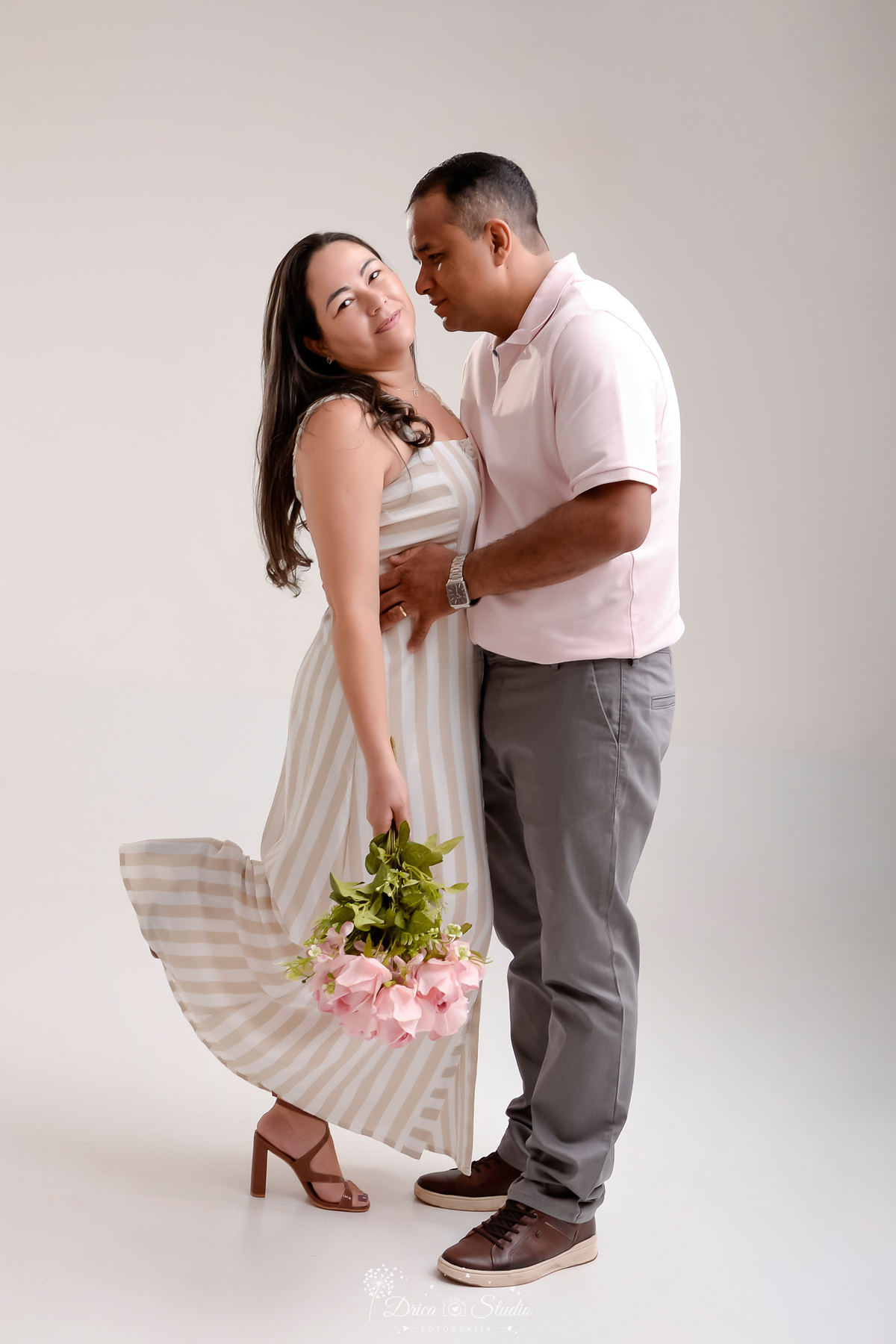 prewedding - ensaio casal - noivos - casamento - ensaio em estudio - drica studio - xinguara - pará - casal abraçados - naiva segurando um buque de rosas - foto em fundo branco - noiva usando vestido longo - noivo usando calça cinza e camisa clara 