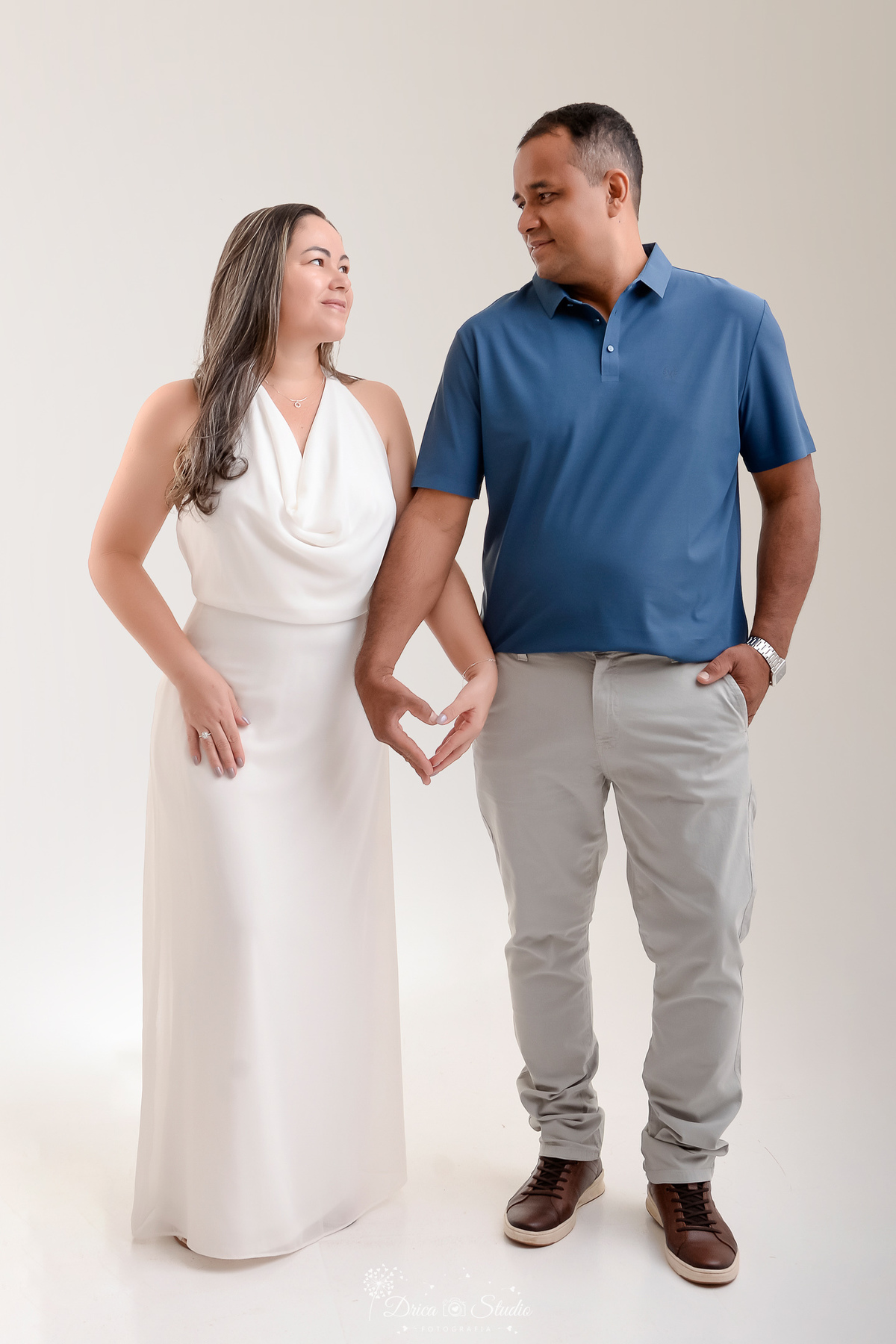 prewedding - ensaio casal - noivos - casamento - ensaio em estudio - drica studio - xinguara - pará - noiva usando vestido branco longo - noivo usando calça cinza e camisa azul - noivos com as mãos fazendo o formato de um coração 