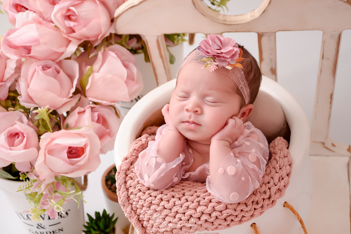 ensaio newborn - recém nascida - 11 dias de vida - drica studio - xinguara - pará - bebê dentro de baldinho - usando bory rosa - ao lado arranjo de flores rosas - laço rosa - com as mãoszinhas no rosto - 