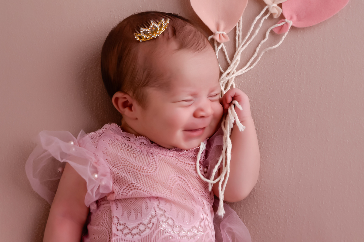 ensaio newborn - recém nascida - 11 dias de vida - drica studio - xinguara - pará - bebê segurando mini balões - com mini coroa na cabeça - sorrindo para a foto 