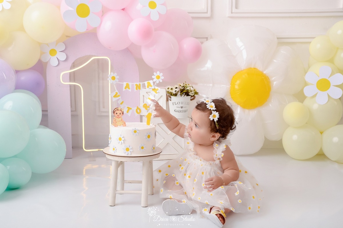 drica studio - smash the cake - 1 aninho - fim de acompanhamento mensal - primeiro contato com o bolo - cenário de margaridas - com balões em tons pasteis - bebe usando vestido branco commargaridas - tiara de margaridas - 