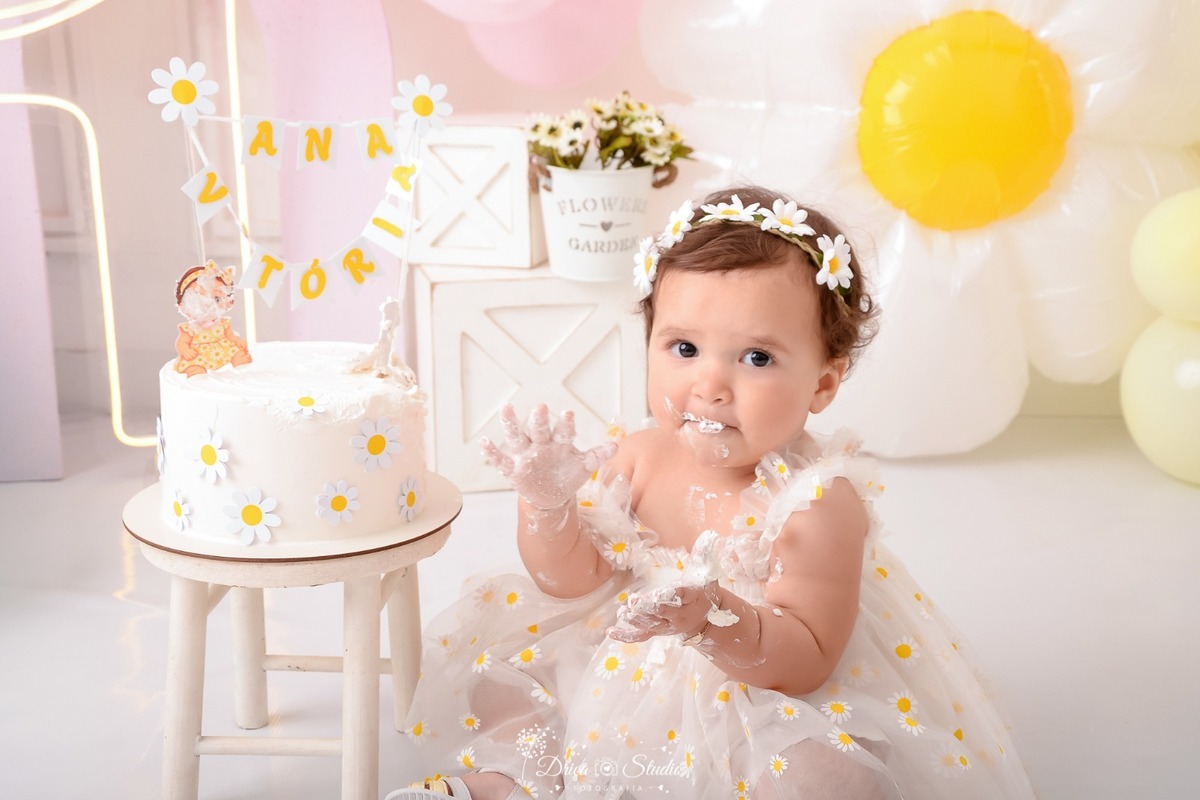 drica studio - smash the cake - 1 aninho - fim de acompanhamento mensal - bebe comendo bolo - balão de margaridas - 1 de led - bolo branco com margaridas - bebê usando vestido branco de margaridas - usando tiara de margaridas 
