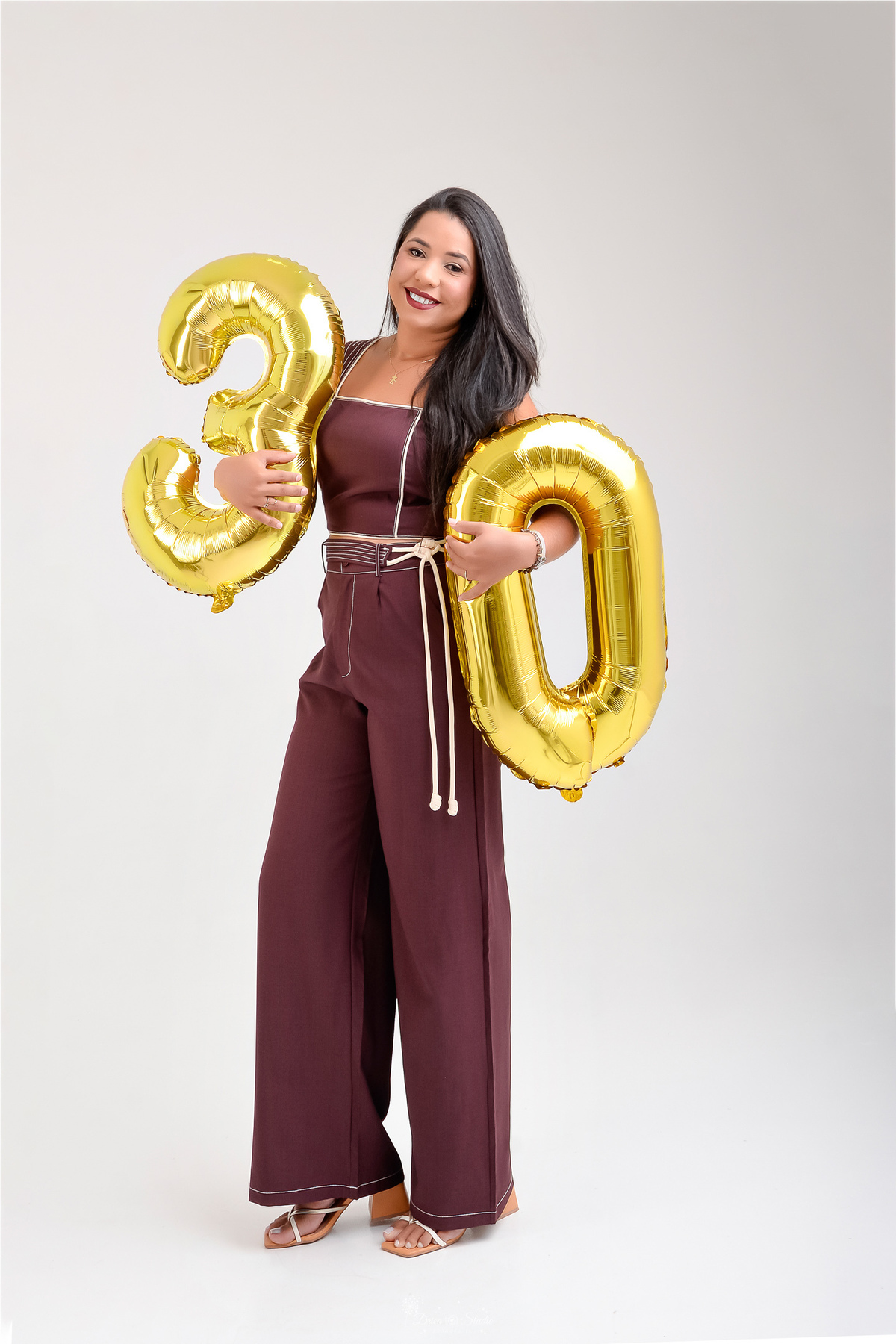 ensaio de aniversario - fotos de 30 anos - ensaio em estudio - drica studio - xinguara - pará - fundo branco - aniversariante em pé - segurando balões de numero 30 - usando conjunto na cor marrom - 