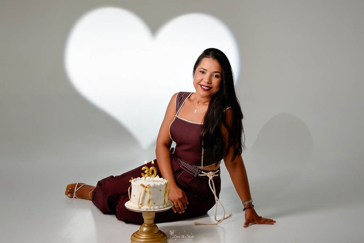 ensaio de aniversario - fotos de 30 anos - ensaio em estudio - drica studio - xinguara - pará - bolo branco com laços dourados - sentada no chão usando conjunto marrom - led com luz de coração ao fundo - 